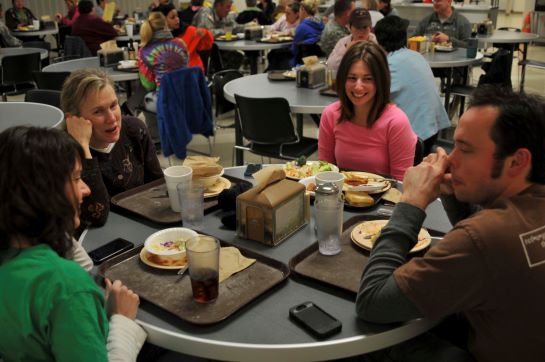 A small group of smiling participants chat over a meal at the chow hall.,